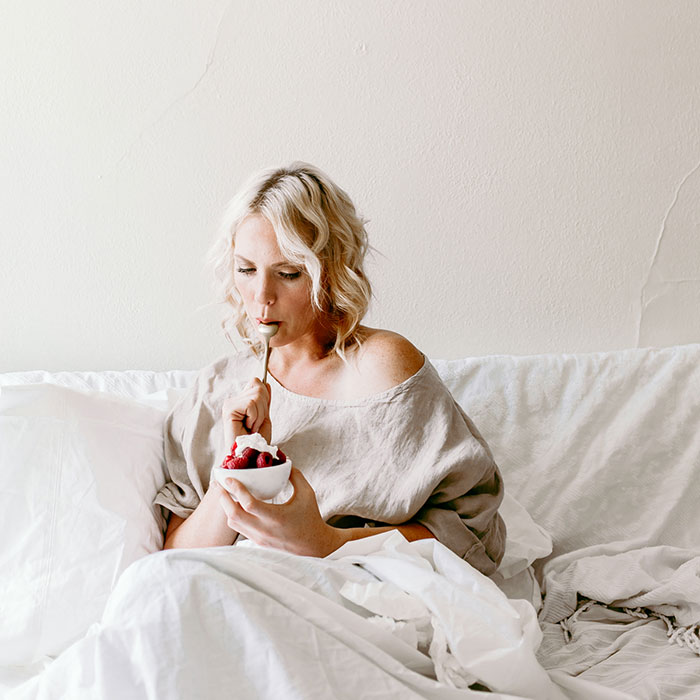 woman in bed eating raspberries with cream