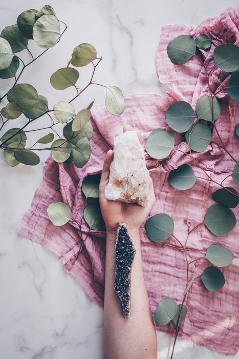 hand holding pink healing crystal and eucalyptus florals around it